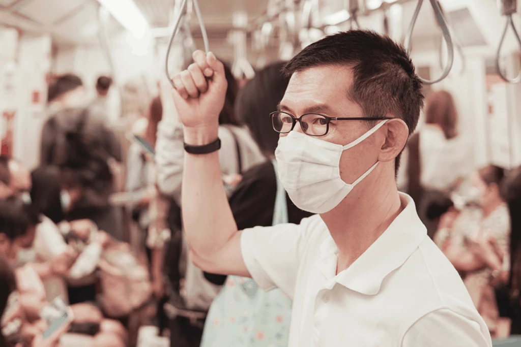 man wearing facemask to prevent covid while on a busy train