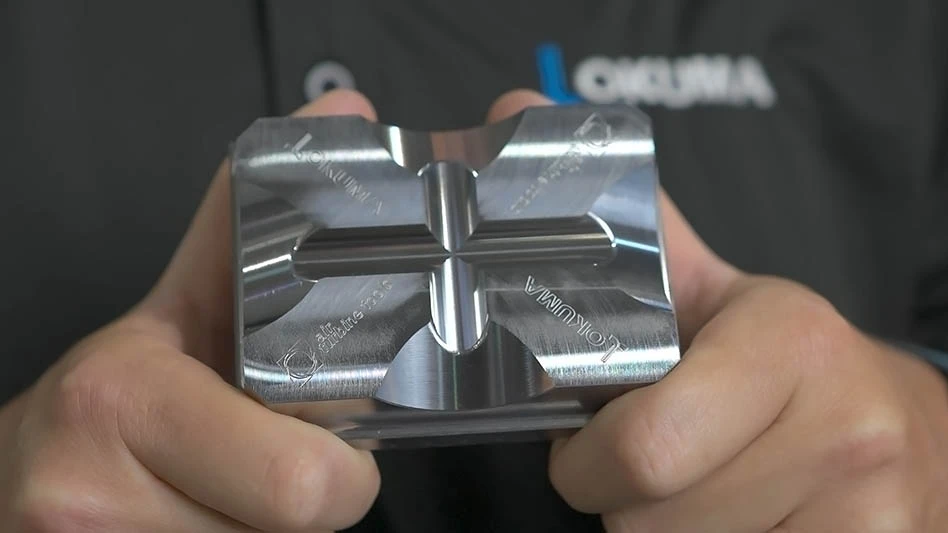 hands holding a shiny metal workpiece carved with air turbine tools and okuma logos