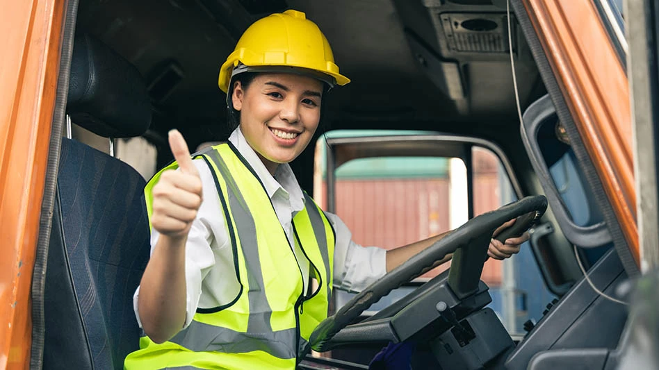 Woman in hard hat gives a thumbs up while sitting in a truck cab