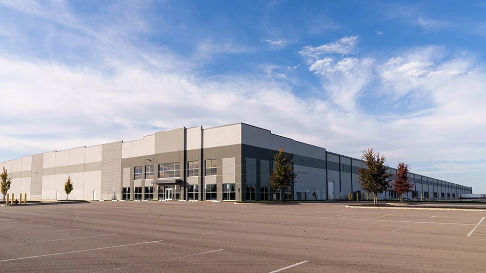 large manufacturing building surrounded by large parking lot, blue sky and clouds