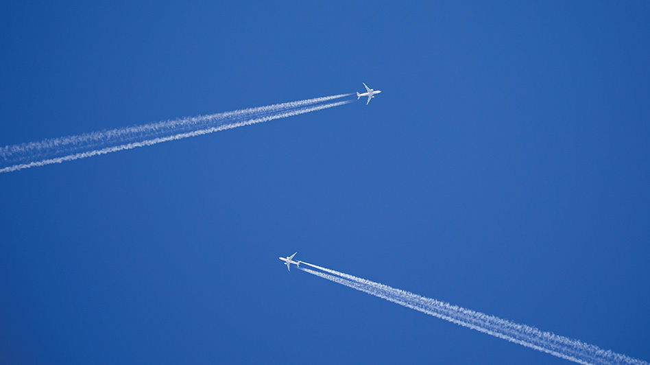 Two white jets flying towards each other with long contrails in front of a blue sky