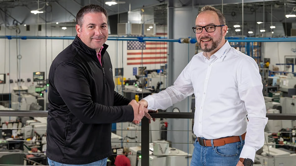 two men shaking hands in front of a factory floor