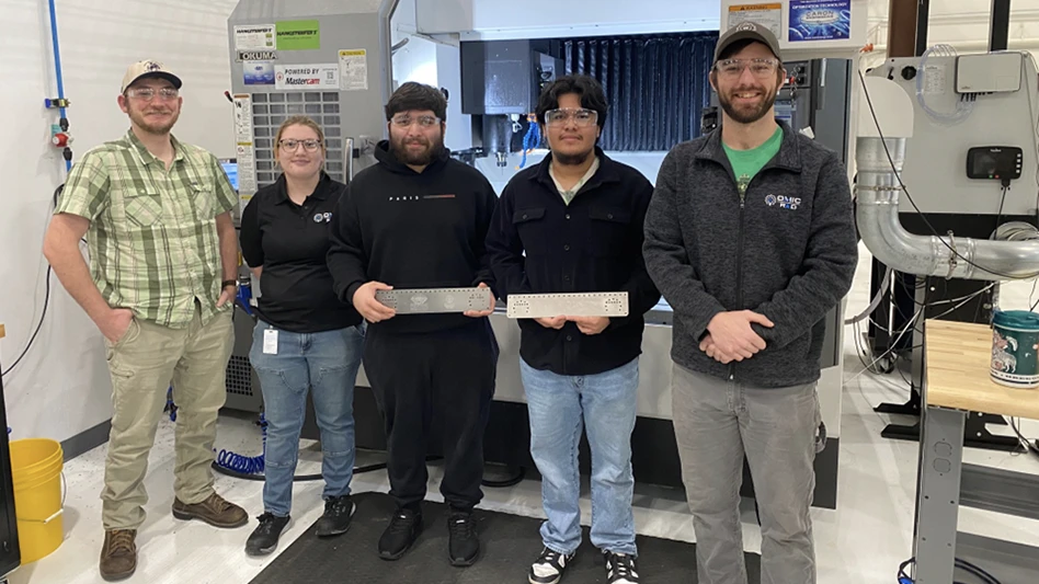 five people standing in front of a machining center, two are holding metal pieces